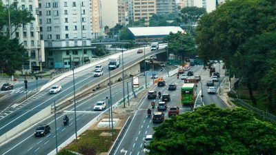 Avenida movimentada em centro urbano com carros, ônibus e prédios ao redor